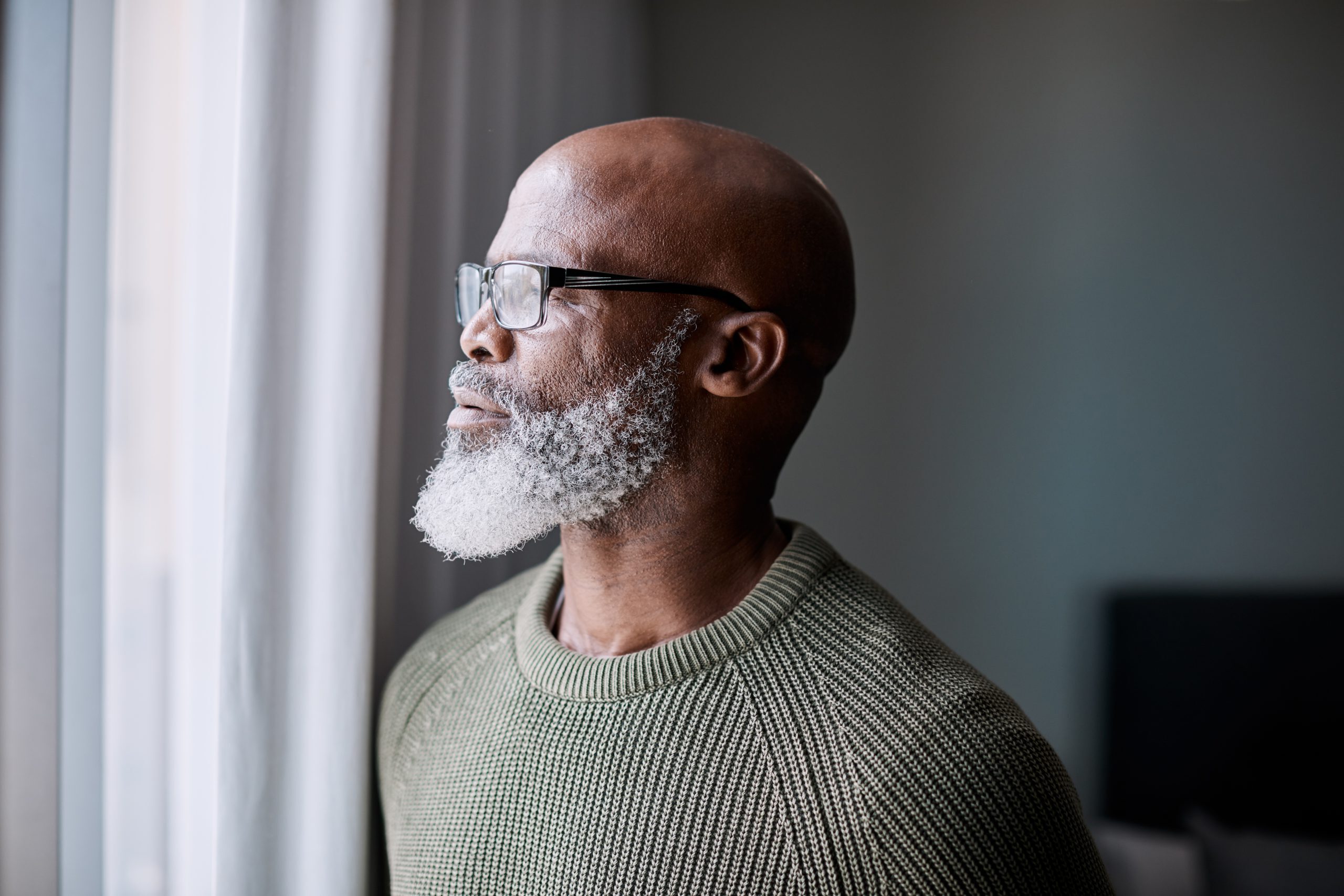 A man with a beard looks out a window. For a better financial future when you can’t work, get help from attorneys for Social Security Disability benefits in Utah.