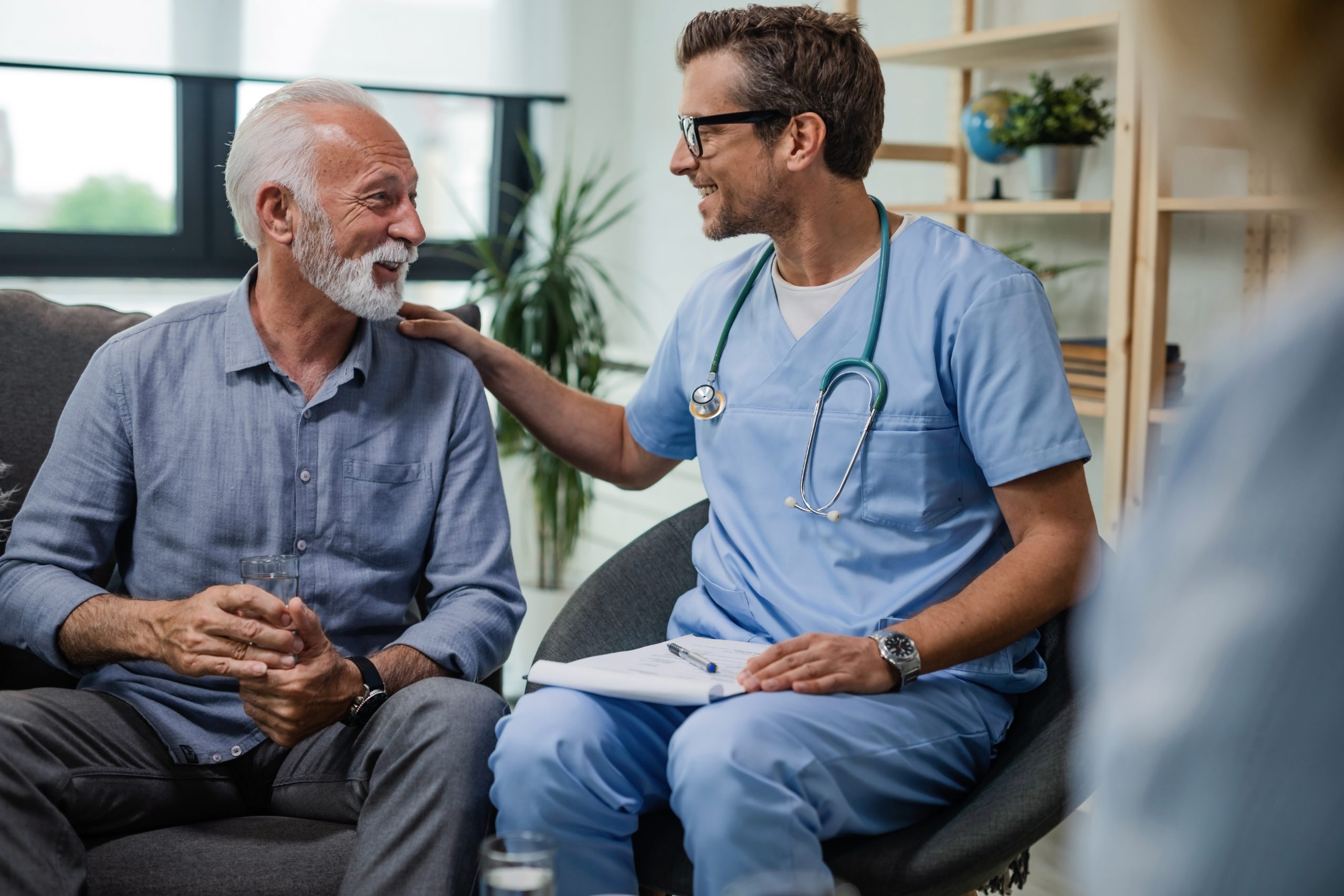 A man sits on couch next to a doctor. The doctor puts his hand on the man's shoulder. When you apply for disability benefits, information from your doctor is important.