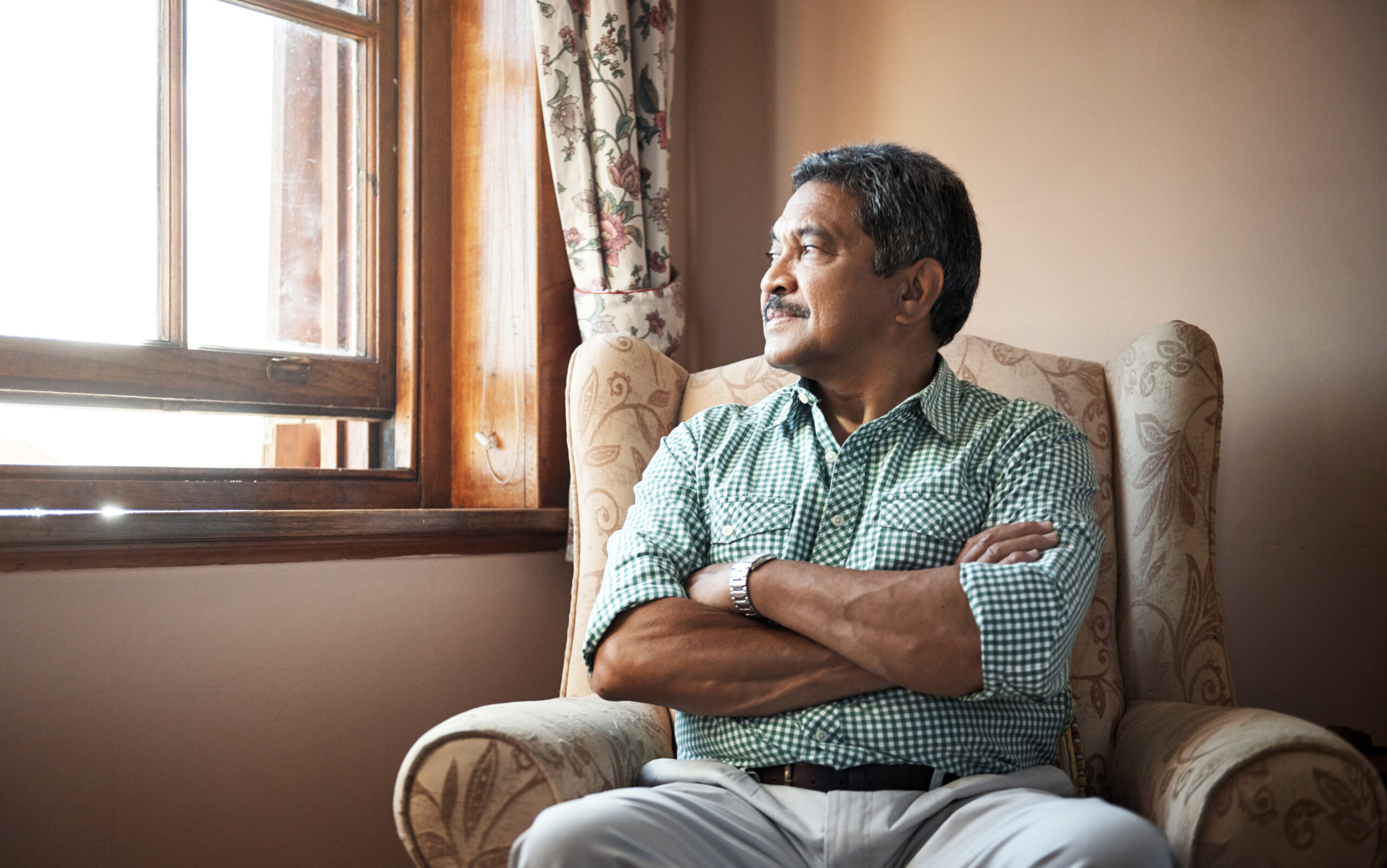 A man sits in an armchair, arms folded, looking to the side out a window. Your next step if you’re denied disability benefits is to appeal.