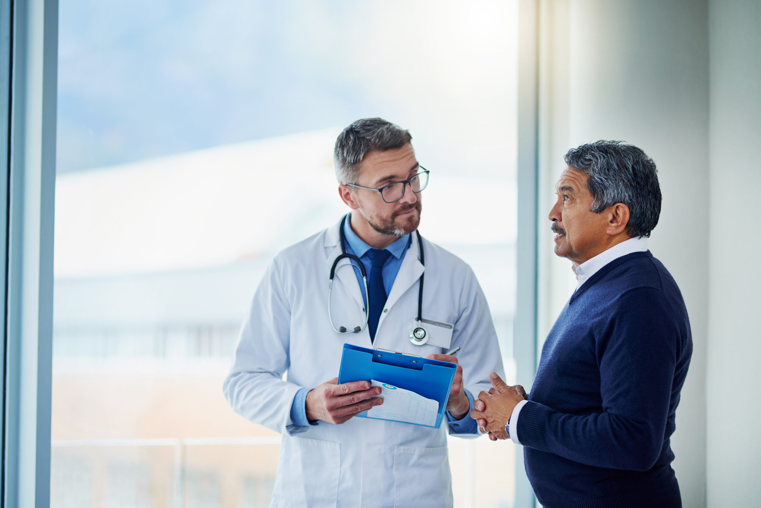 A man talks to a doctor as they stand in front of a clinic window. Appealing a denied disability claim involves getting more information and evidence from doctors.