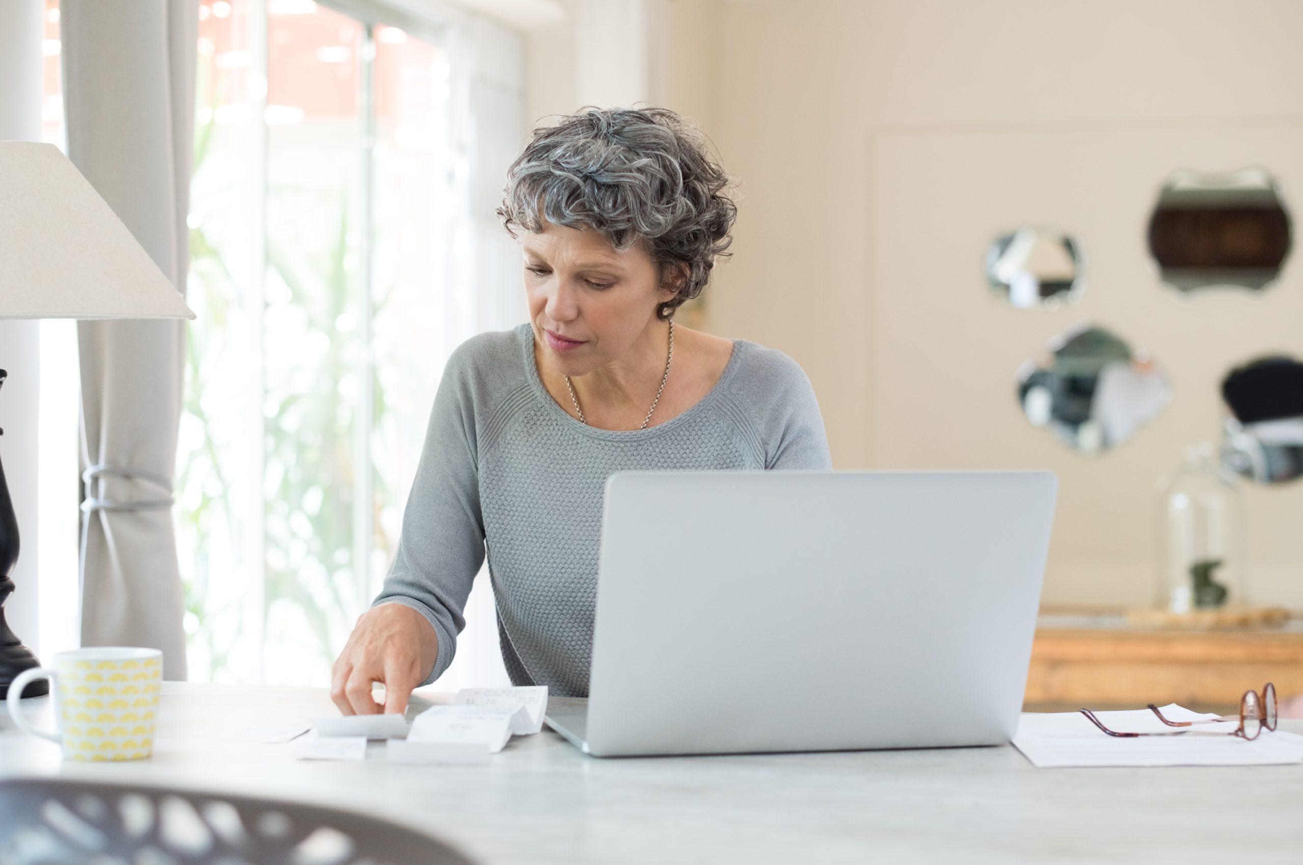 A woman sits at a kitchen counter, notes and laptop in front of her. Finances and work history are part of the requirements for disability benefits.