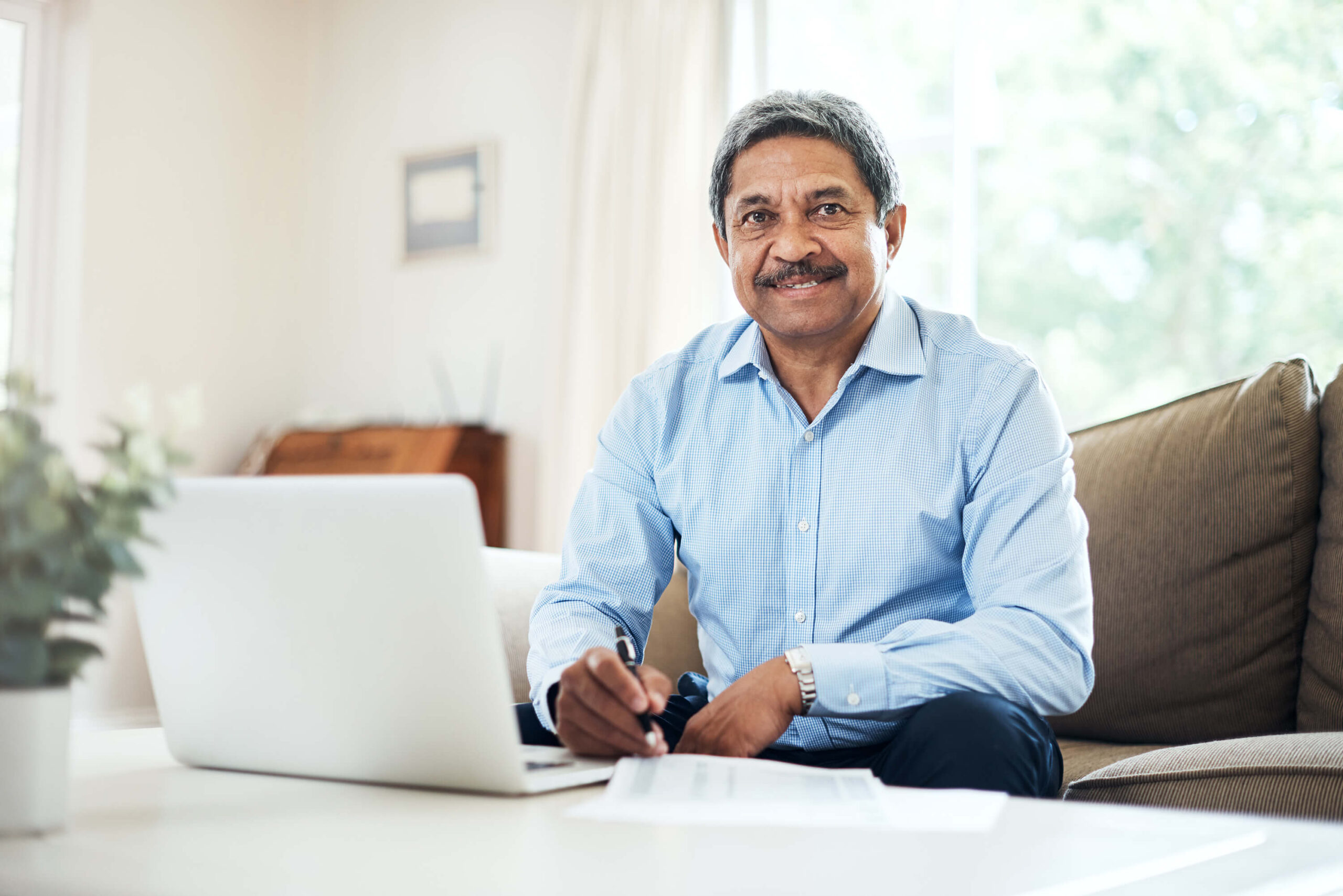 Holding pen over paper, a man looks up from his couch and smiles at the camera. Barnes SSD lawyers help you decide if you qualify, apply, and appeal denials of disability benefits.