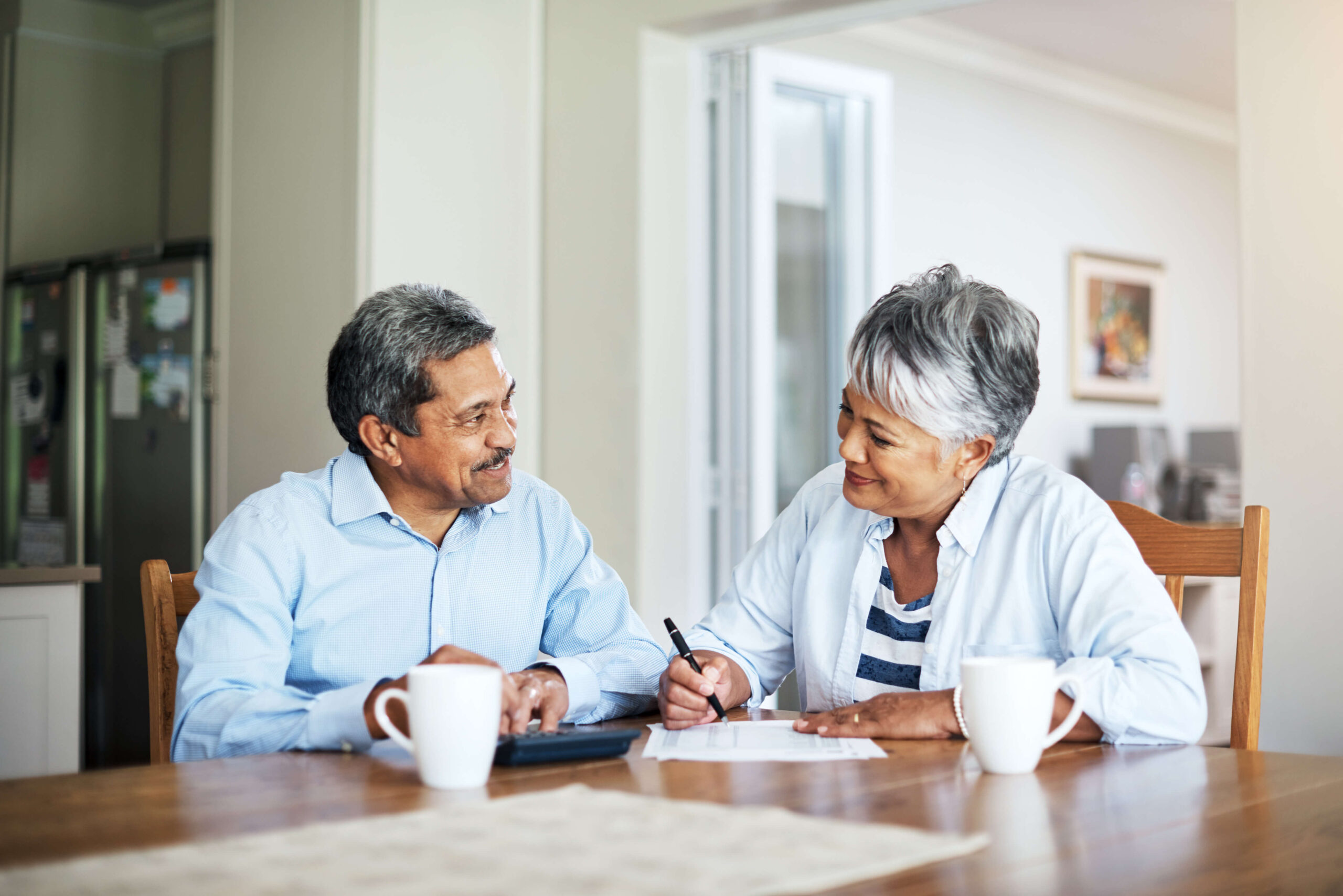 A man and woman sit at a dining room table over paperwork, grinning at each other. Barnes disability attorneys provide personal attention for your disability benefits claim.