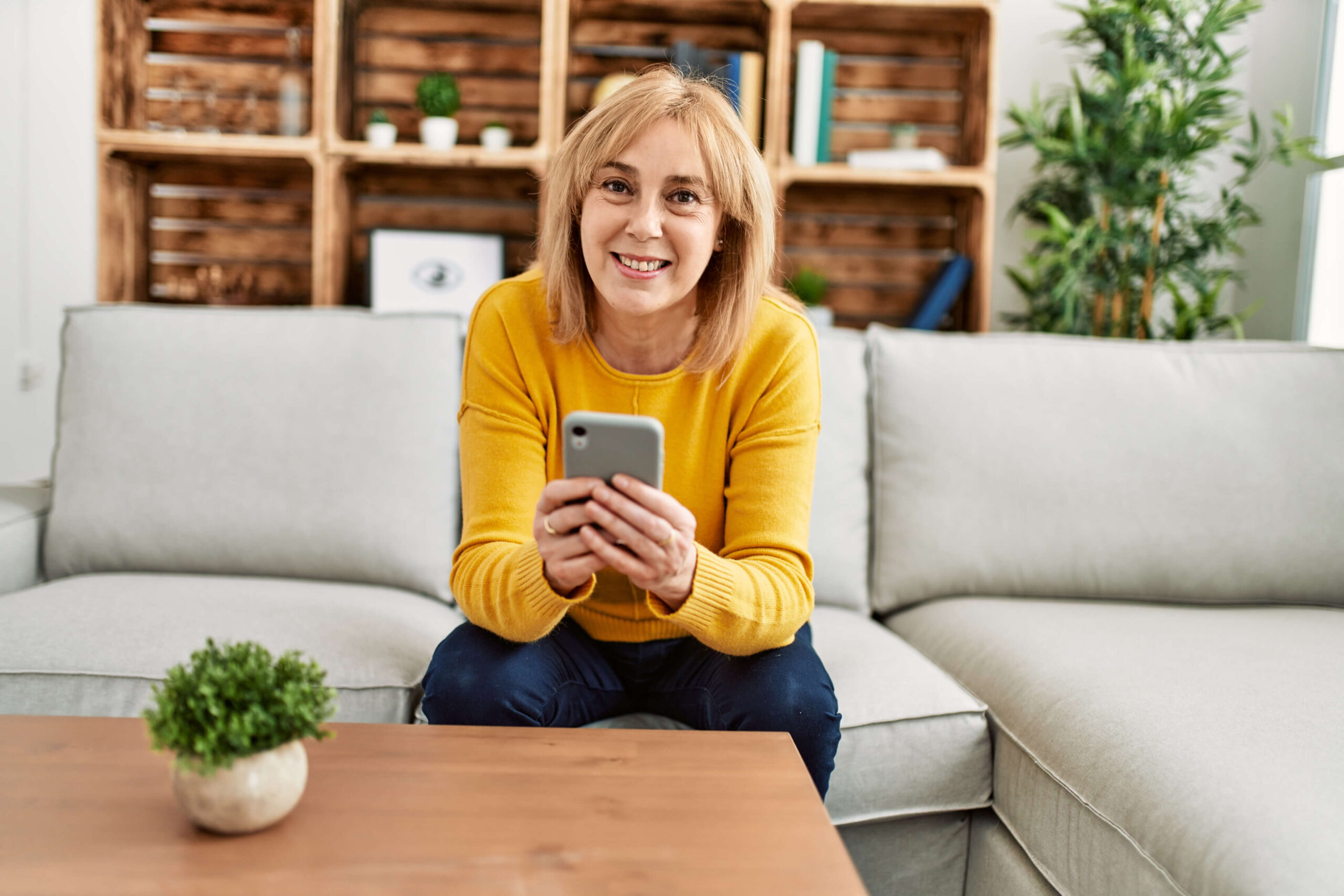 A woman sitting on her couch looks up from her phone and smiles. Barnes disability attorneys in St. George can make the experience of seeking disability benefits better.