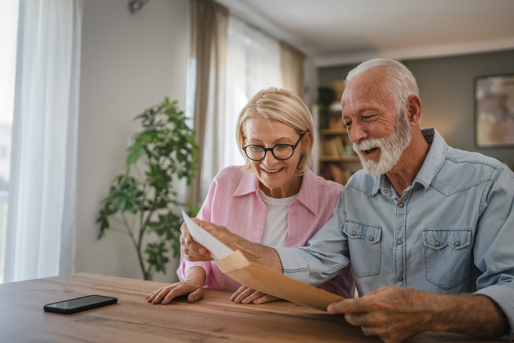 A woman and man sit at a wooden dining room table. The man pulls a paper out of a large envelope. The SSD attorneys at Barnes Disability guide you through your benefits paperwork.